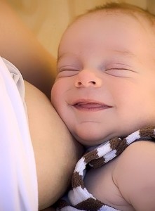 малыш сыто улыбается возле маминой груди