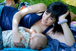 молодая мама кормит ребенка грудью, лежа на травке